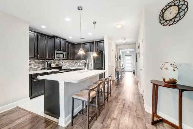 a kitchen with stainless steel appliances granite countertop a refrigerator a sink dishwasher a stove and a dining table with wooden floor