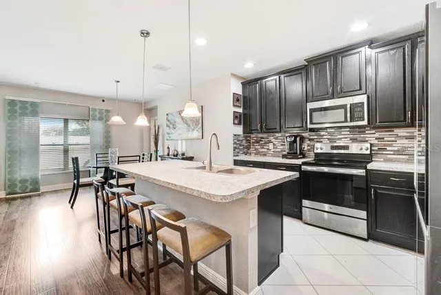 a kitchen with stainless steel appliances kitchen island granite countertop a stove a sink a oven a dining table and chairs with wooden floor