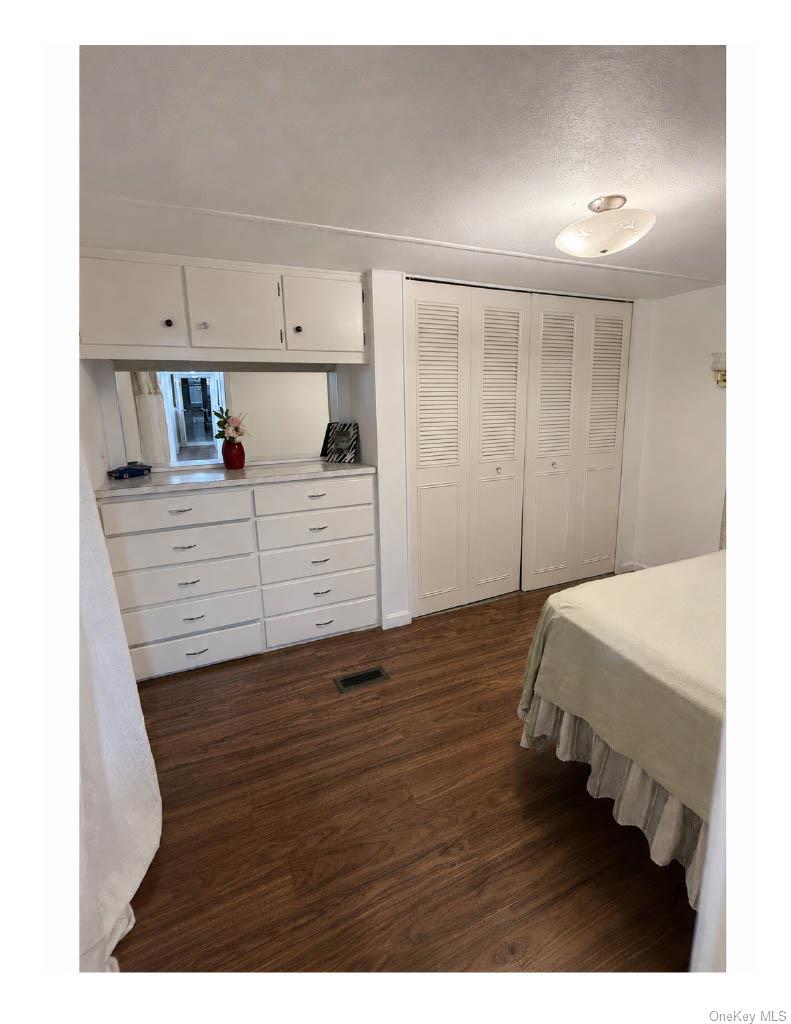 136 Quaker Rd Park Pomona, NY 10970 - Photo 22 of 24 Bedroom 3 Integrated dresser and cabinetry with mirror, wood-finish flooring, white louvered bifold closet doors, and flush-mount ceiling lighting