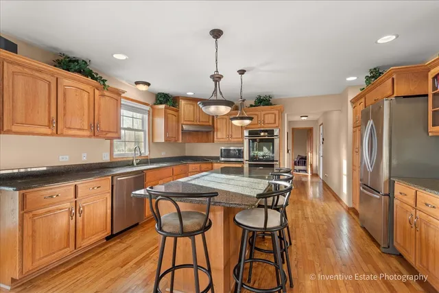 a kitchen with stainless steel appliances kitchen island granite countertop a table chairs in it and wooden floors