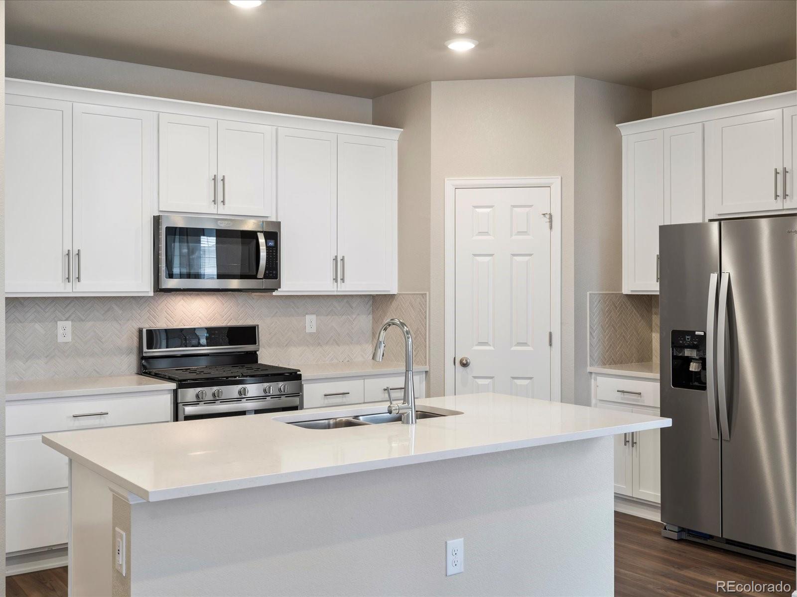a kitchen with stainless steel appliances a stove a microwave a sink a refrigerator and white cabinets