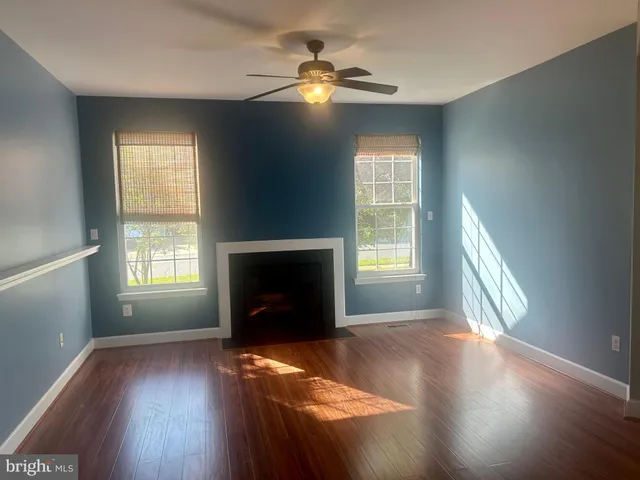 a view of an empty room with wooden floor fireplace and a window