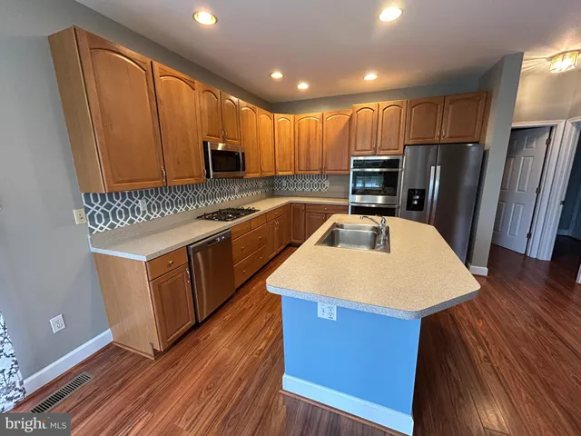 a kitchen with kitchen island granite countertop wooden cabinets a refrigerator a stove a sink and dishwasher with wooden floor