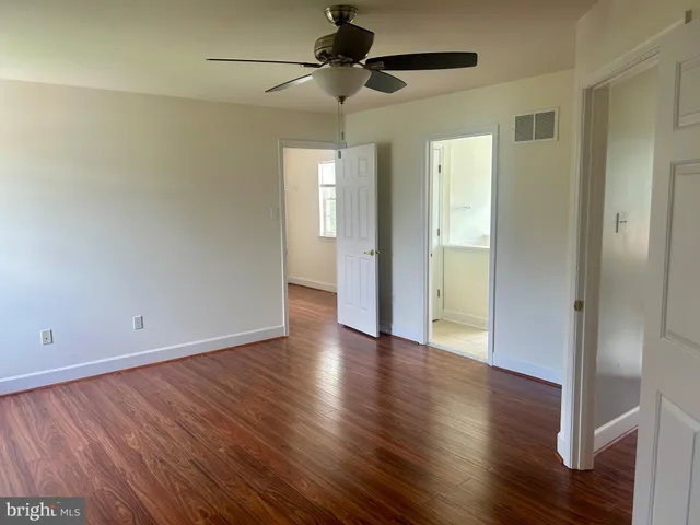an empty room with wooden floor a ceiling fan and windows