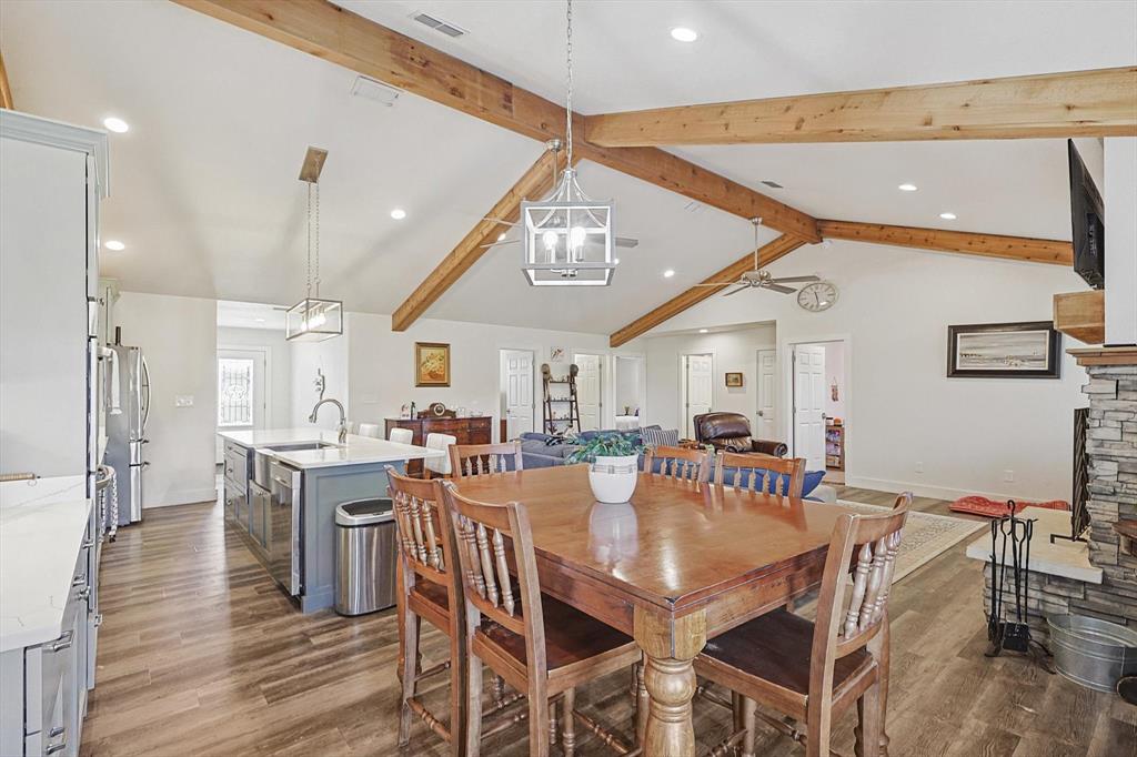 1161 Lynn Creek Road Jacksboro, TX 76458 - Photo 16 of 40 Dining room with dark wood-type flooring, sink, an inviting chandelier, vaulted ceiling with beams, and a stone fireplace