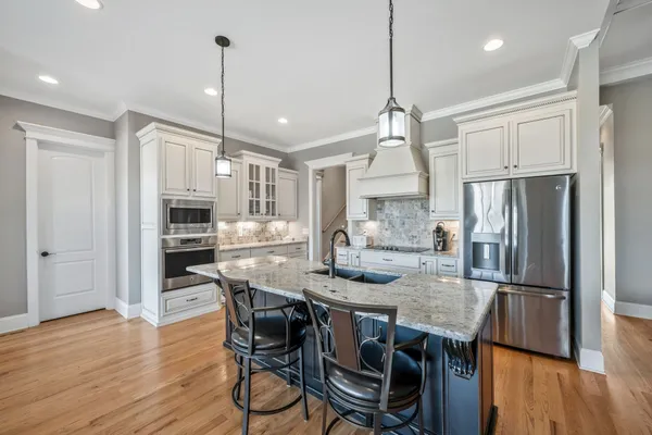 a kitchen with stainless steel appliances granite countertop a refrigerator a stove a kitchen island a dining table and wooden floor