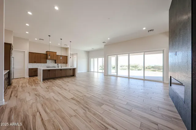 a view of an empty room and kitchen view with wooden floor