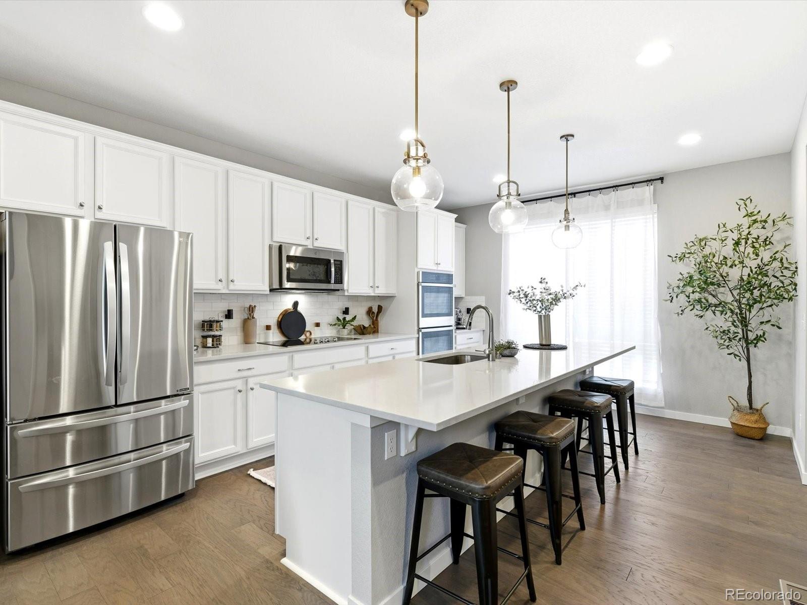 8338 Rivulet Point Highlands Ranch, CO 80129 - Photo 11 of 50 a kitchen with granite countertop a refrigerator a stove a microwave oven a sink a dining table and chairs with wooden floor