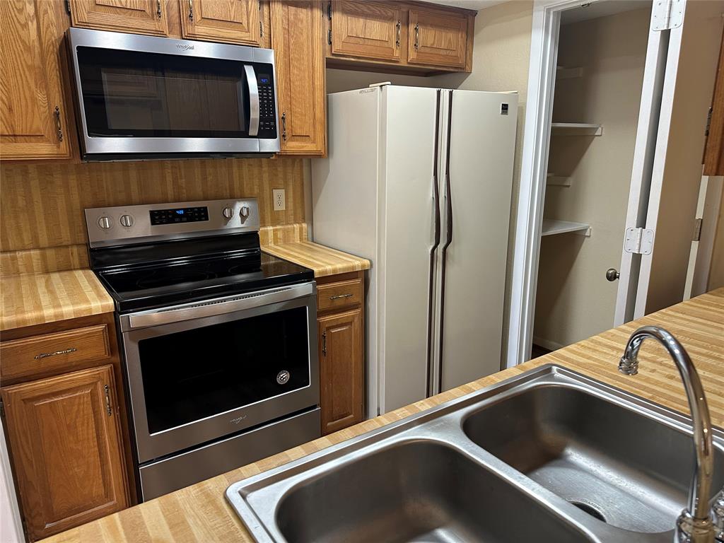927 Signal Ridge Place Rockwall, TX 75032 - Photo 10 of 16 Stainless steel microwave and range, wood-finish countertops, wood cabinetry, and a double basin stainless steel sink with a chrome faucet