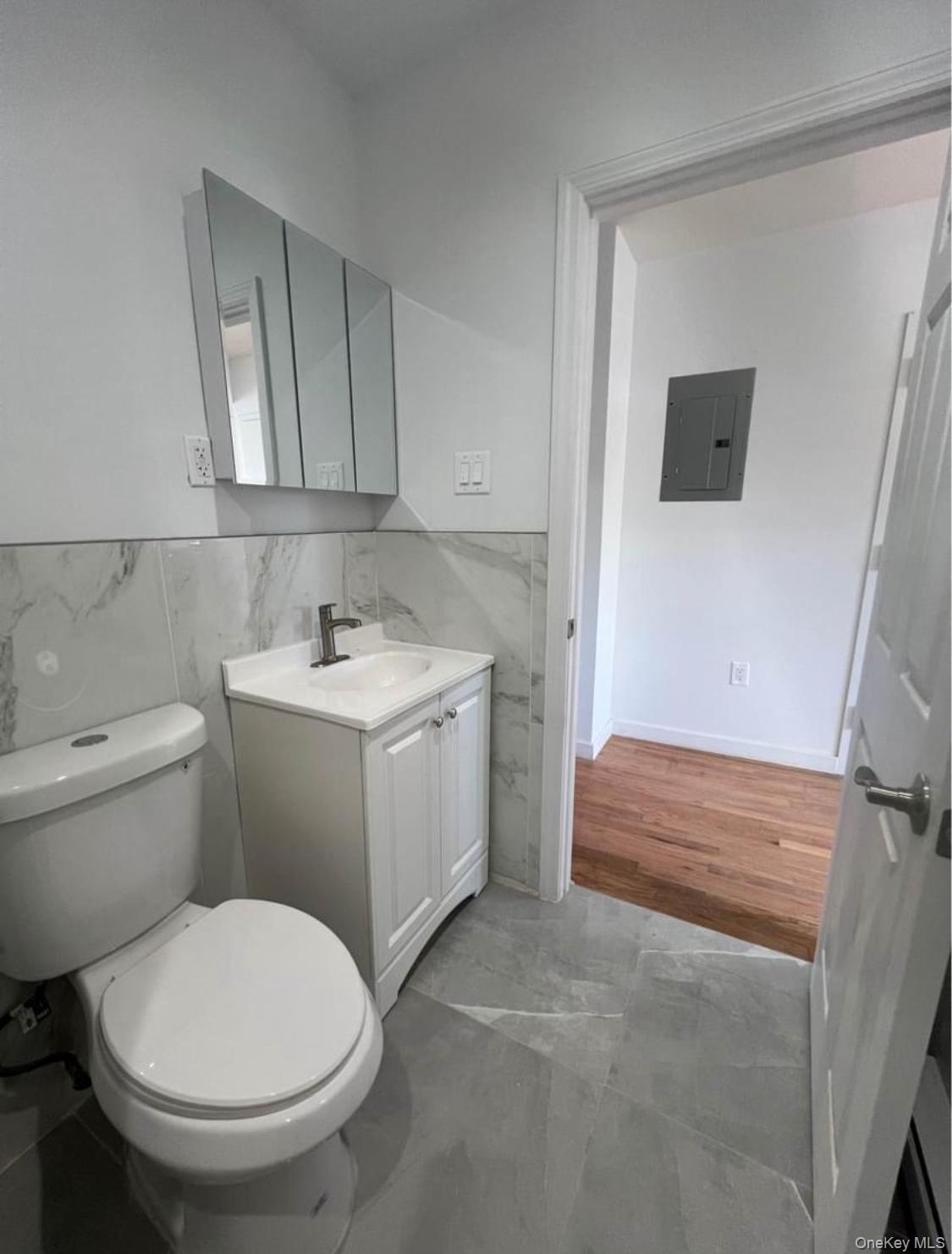 718 Rosedale Avenue Bronx, NY 10473 - Photo 5 of 9 Half bath featuring tile walls, vanity, electric panel, wainscoting, and light tile patterned floors