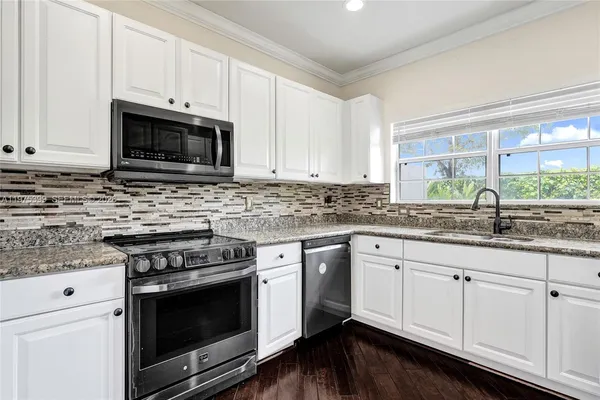 a kitchen with granite countertop white cabinets appliances a sink and a window