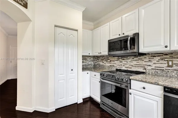a kitchen with granite countertop white cabinets stainless steel appliances and wooden floor