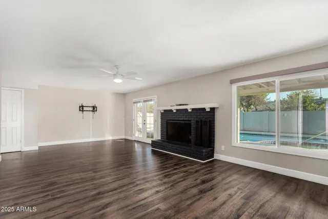 an empty room with wooden floor fire place and windows