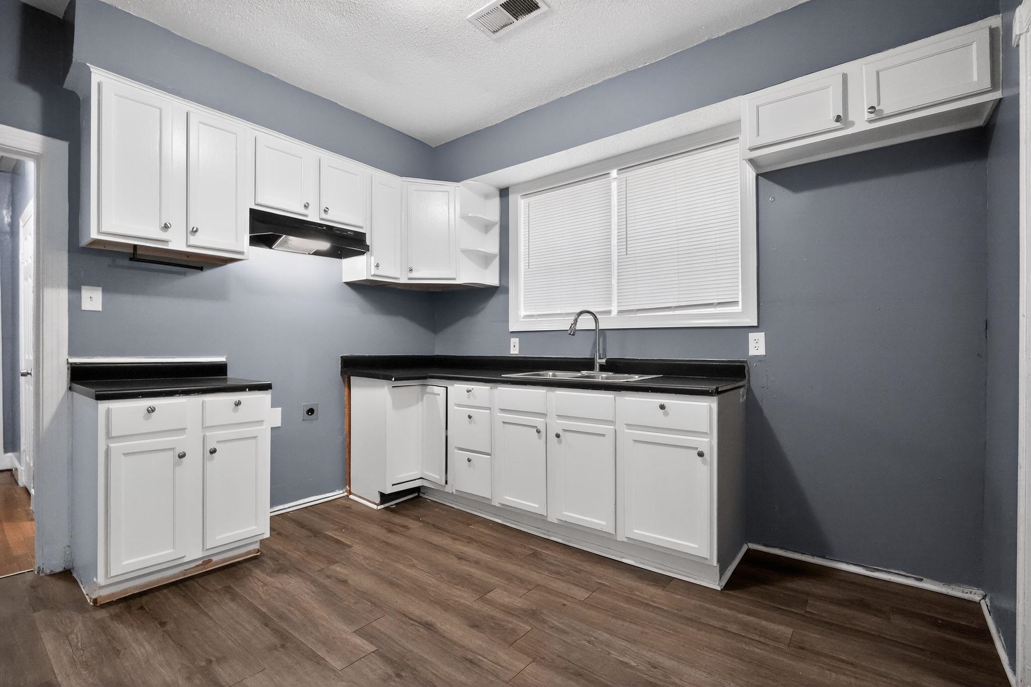 4199 Auburn Road Memphis, TN 38116 - Photo 21 of 32 Kitchen featuring wood-finish flooring, white cabinetry, dark countertops, a window with blinds, and a double-basin sink with a gooseneck faucet