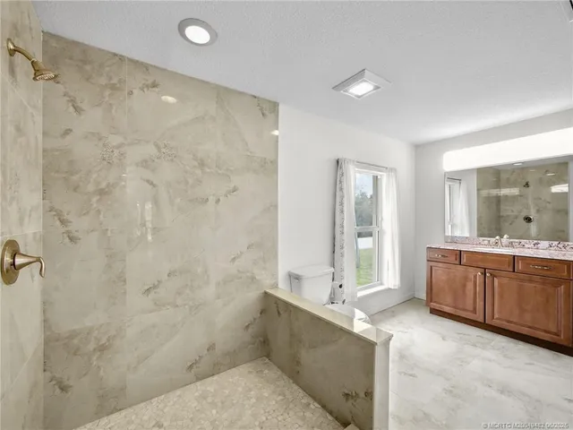 a bathroom with a granite countertop sink a toilet a mirror and shower