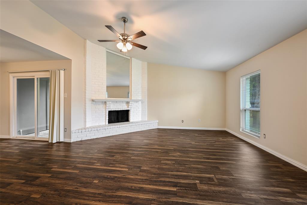 7318 Emory Oak Lane Dallas, TX 75249 - Photo 9 of 28 Spacious living area featuring wood-finish flooring, a white brick fireplace with a hearth, and a ceiling fan with integrated lighting