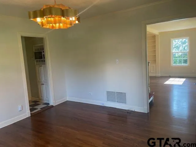 an empty room with wooden floor chandelier and windows