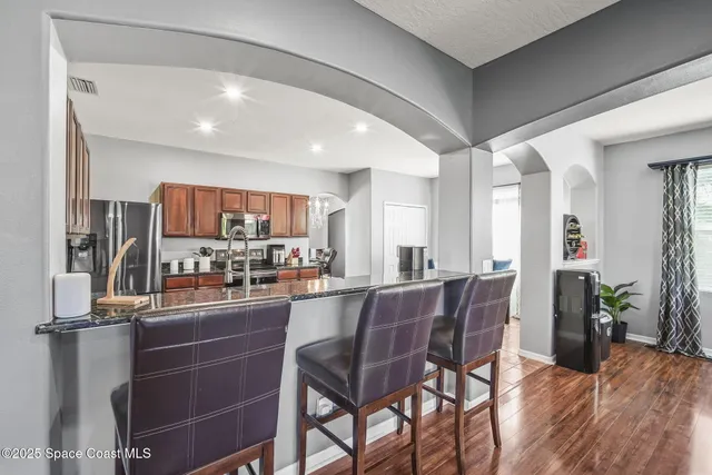 a kitchen with stainless steel appliances granite countertop a stove top oven a sink dishwasher a dining table and chairs with wooden floor