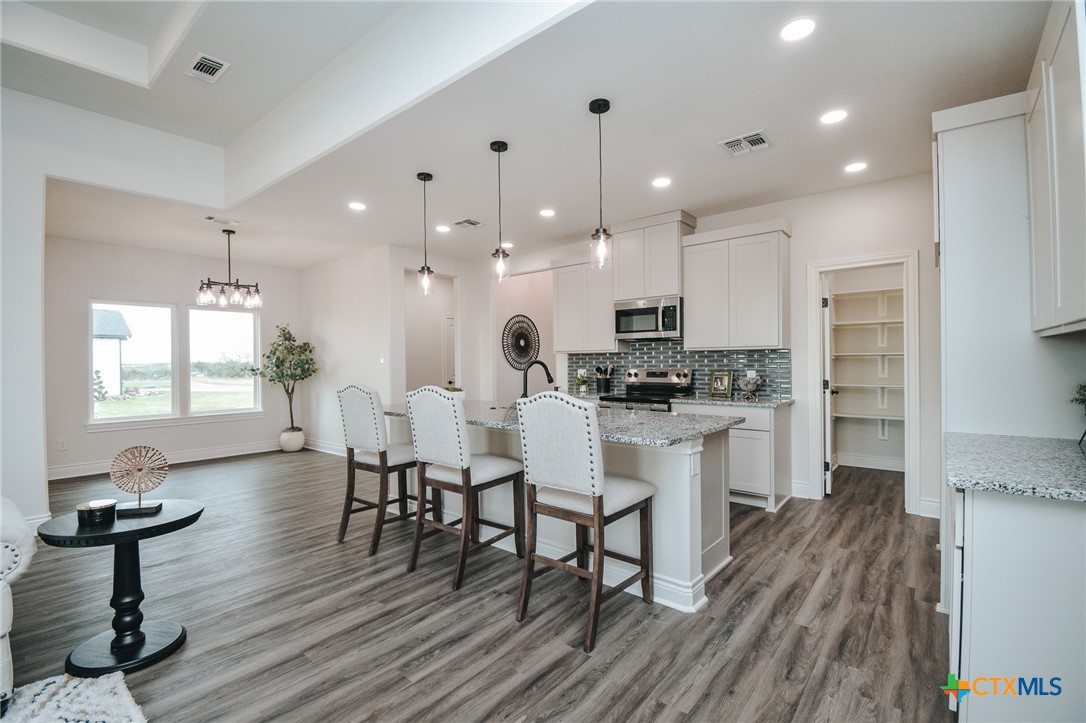 321 Whitetail Lane Victoria, TX 77905 - Photo 7 of 47 a kitchen with stainless steel appliances kitchen island granite countertop a stove a refrigerator and a dining table with wooden floors