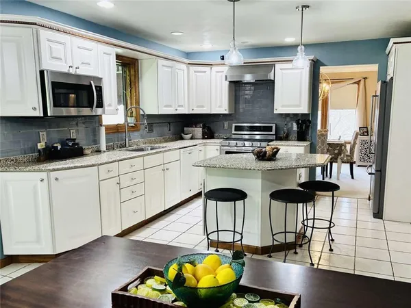 a kitchen with stainless steel appliances granite countertop a stove top oven a sink a dining table and chairs with wooden floor