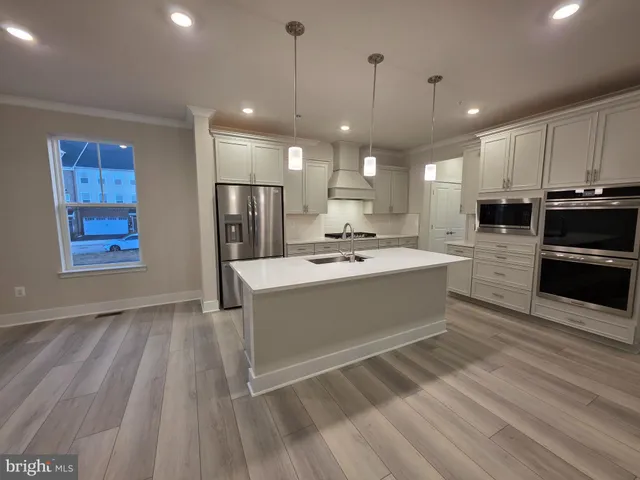 a large white kitchen with kitchen island a sink dishwasher a stove and a refrigerator with wooden floor