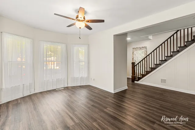 a view of an empty room with wooden floor and a ceiling fan