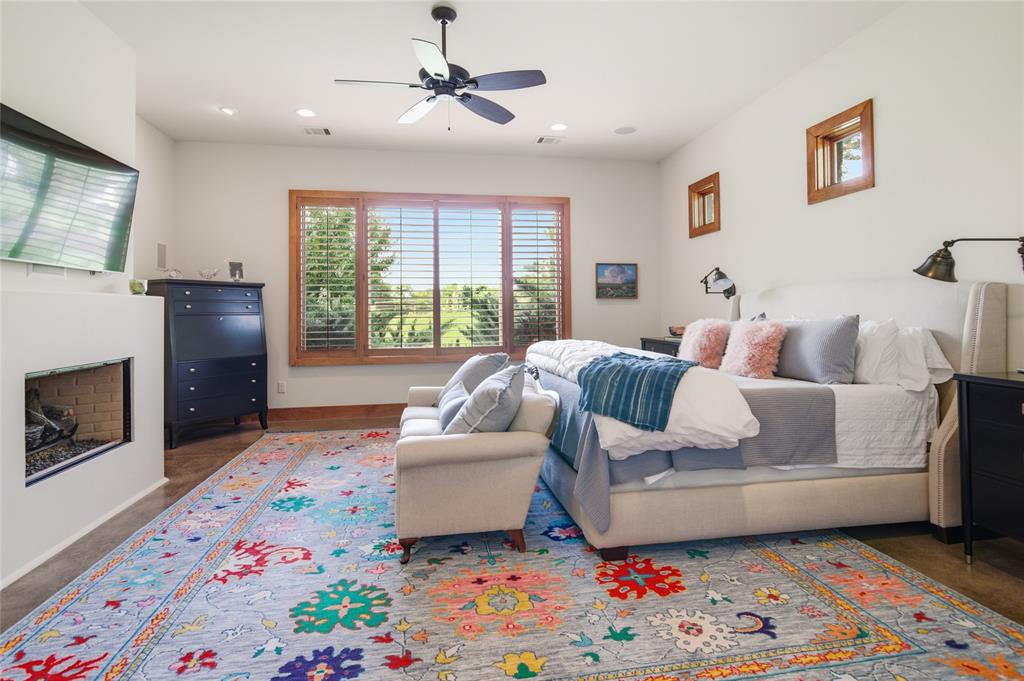 1138 Bancroft Road Keller, TX 76248 - Photo 17 of 39 Spacious bedroom featuring large windows with wood trim, a built-in fireplace, concrete flooring, and a ceiling fan with integrated lighting
