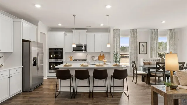 a kitchen with stainless steel appliances kitchen island granite countertop a stove a sink a refrigerator and white cabinets with wooden floor