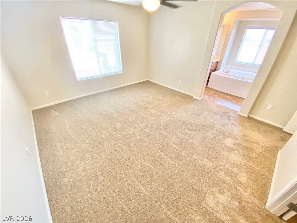 8569 Rhamus Court Las Vegas, NV 89149 - Photo 24 of 35 A spacious primary bedroom featuring plush carpeting and an arched entry leading to a serene bath area.