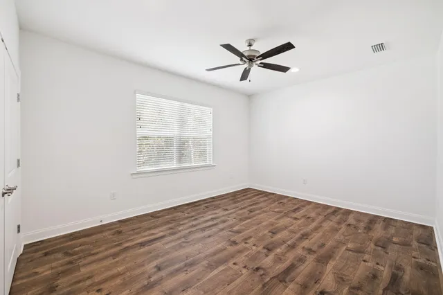an empty room with wooden floor fan and windows
