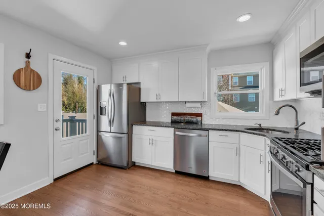 a kitchen with stainless steel appliances granite countertop a stove a sink dishwasher a refrigerator and white cabinets with wooden floor