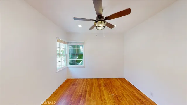 an empty room with wooden floor fan and windows