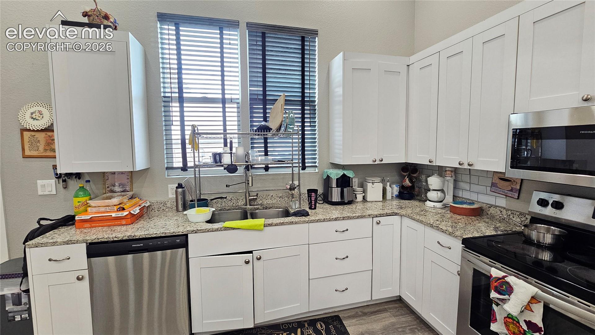 3835 Sengbeil Road Yoder, CO 80864 - Photo 15 of 48 Kitchen featuring white shaker-style cabinetry with brushed nickel hardware, light-toned granite countertops, a subway tile backsplash, and stainless steel appliances including a built-in microwave and dishwasher