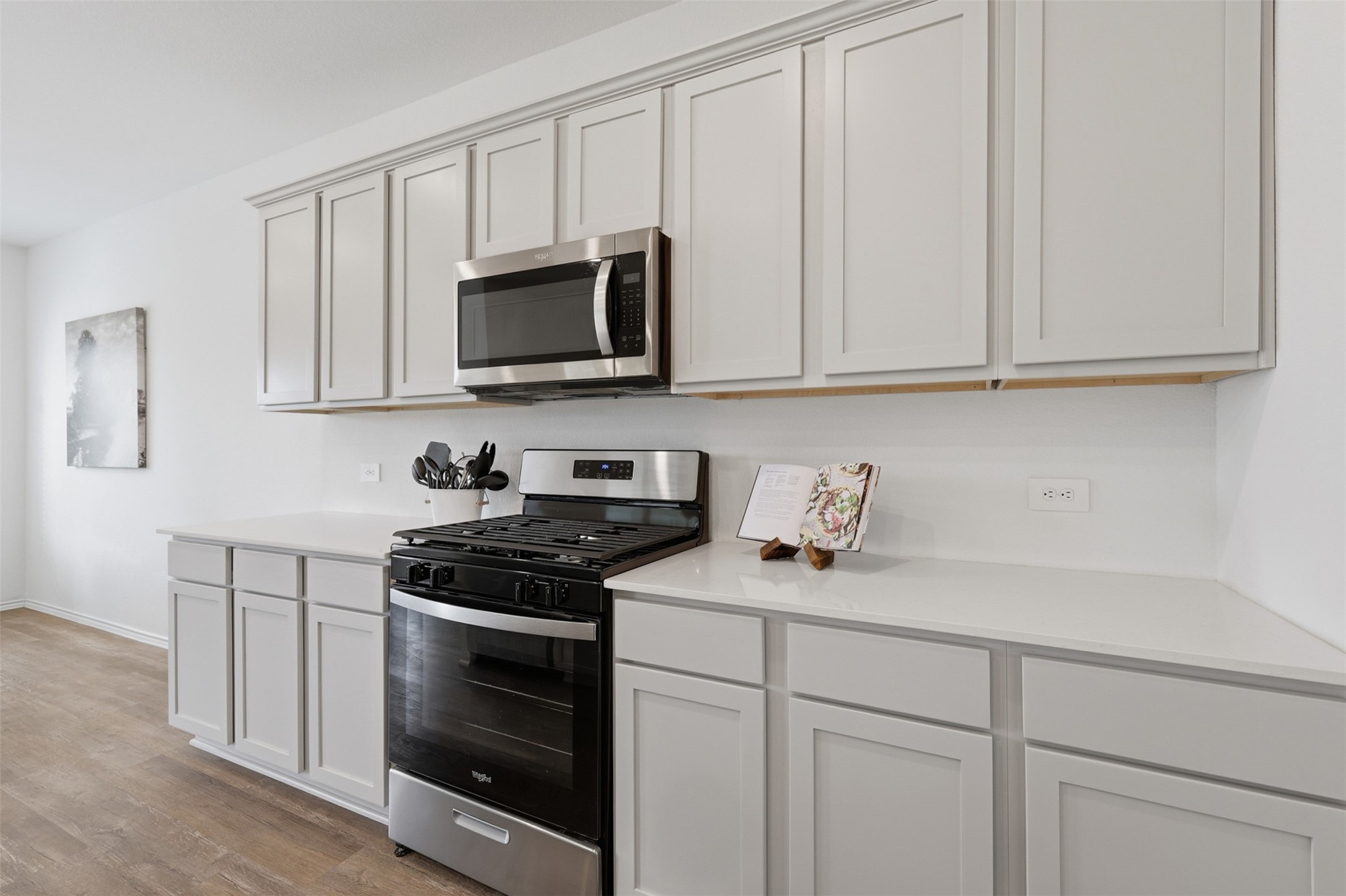 17719 Winfall Drive Crosby, TX 77532 - Photo 11 of 47 Modern kitchen with sleek white cabinetry, stainless steel appliances, including a gas stove and microwave, and ample countertop space for cooking and storage.