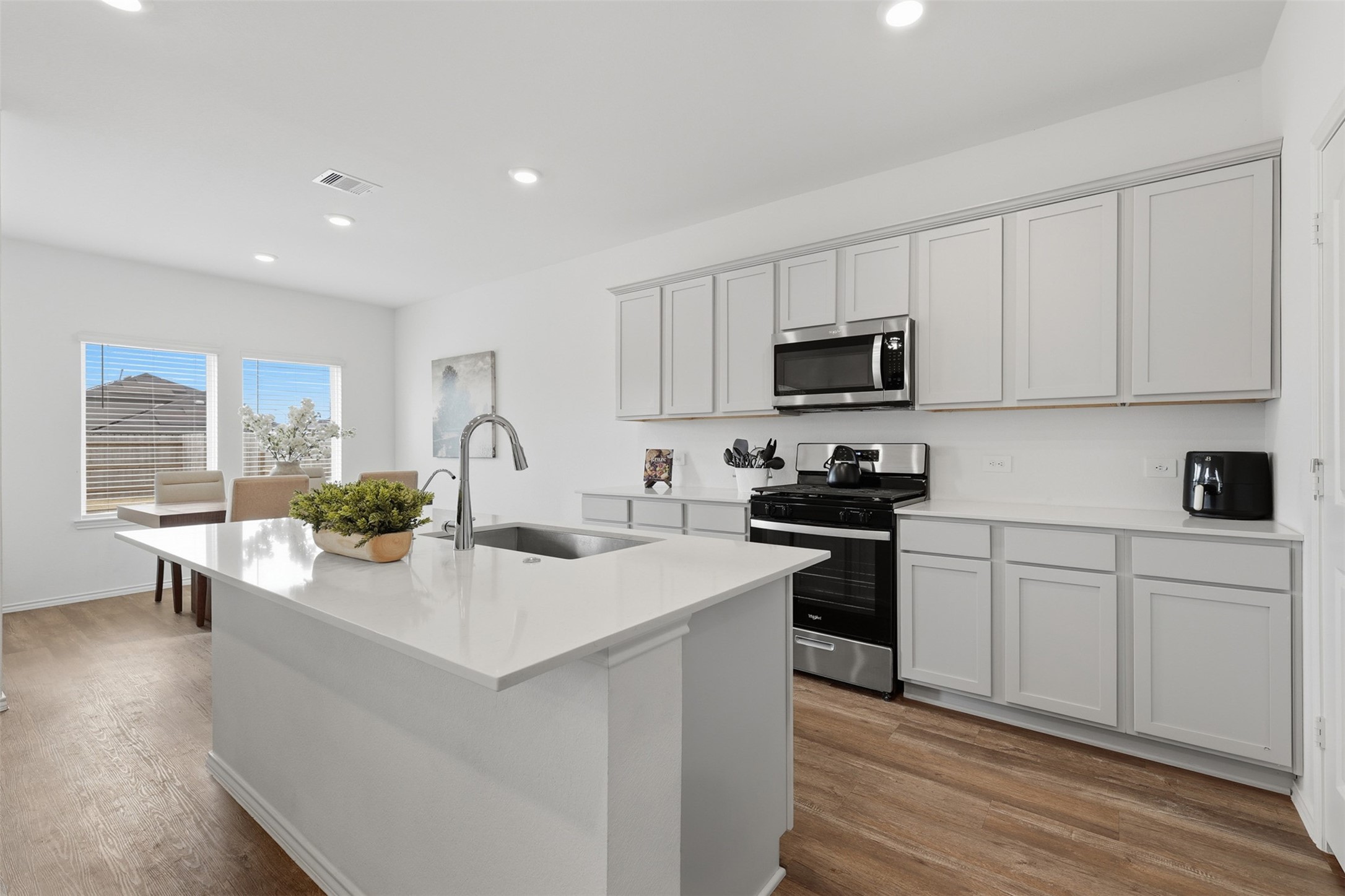 17719 Winfall Drive Crosby, TX 77532 - Photo 14 of 47 This kitchen features modern appliances, light gray cabinetry, and a spacious island with a sink. Natural light floods the space from large windows, complementing the open layout. Perfect for cooking and entertaining.