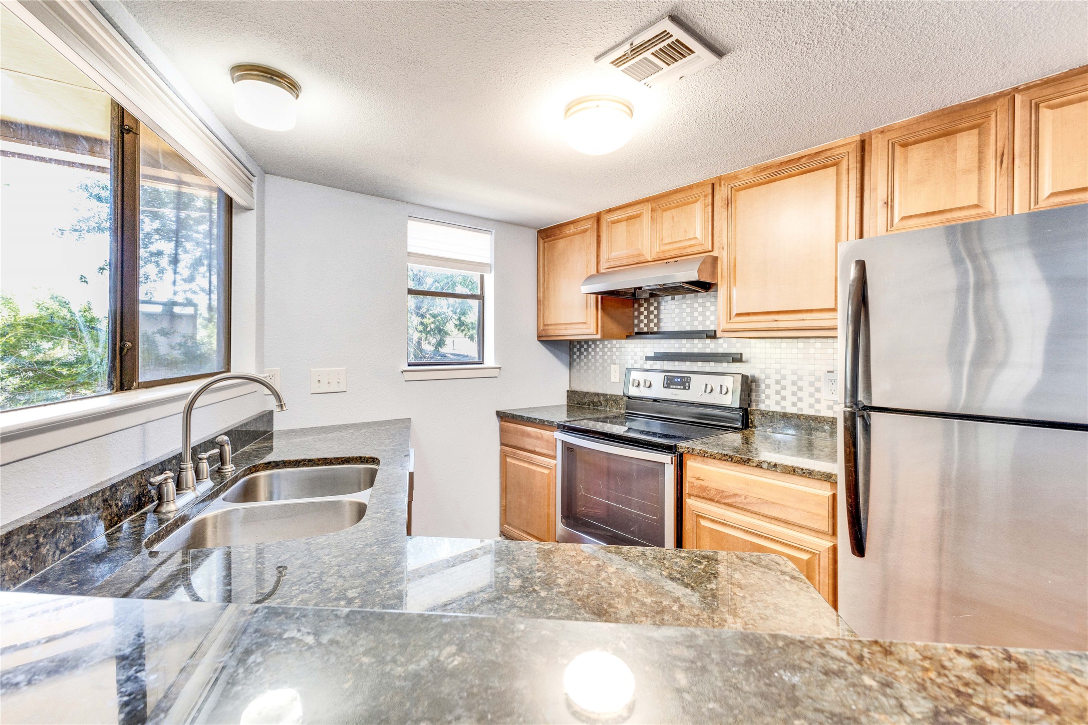 2500 Burleson Road, Unit 703 Austin, TX 78741 - Photo 13 of 24 Polished stone countertops pair with wood cabinets and stainless steel appliances in this kitchen.