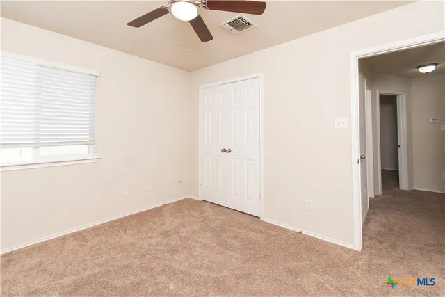 an empty room with a ceiling fan and carpet