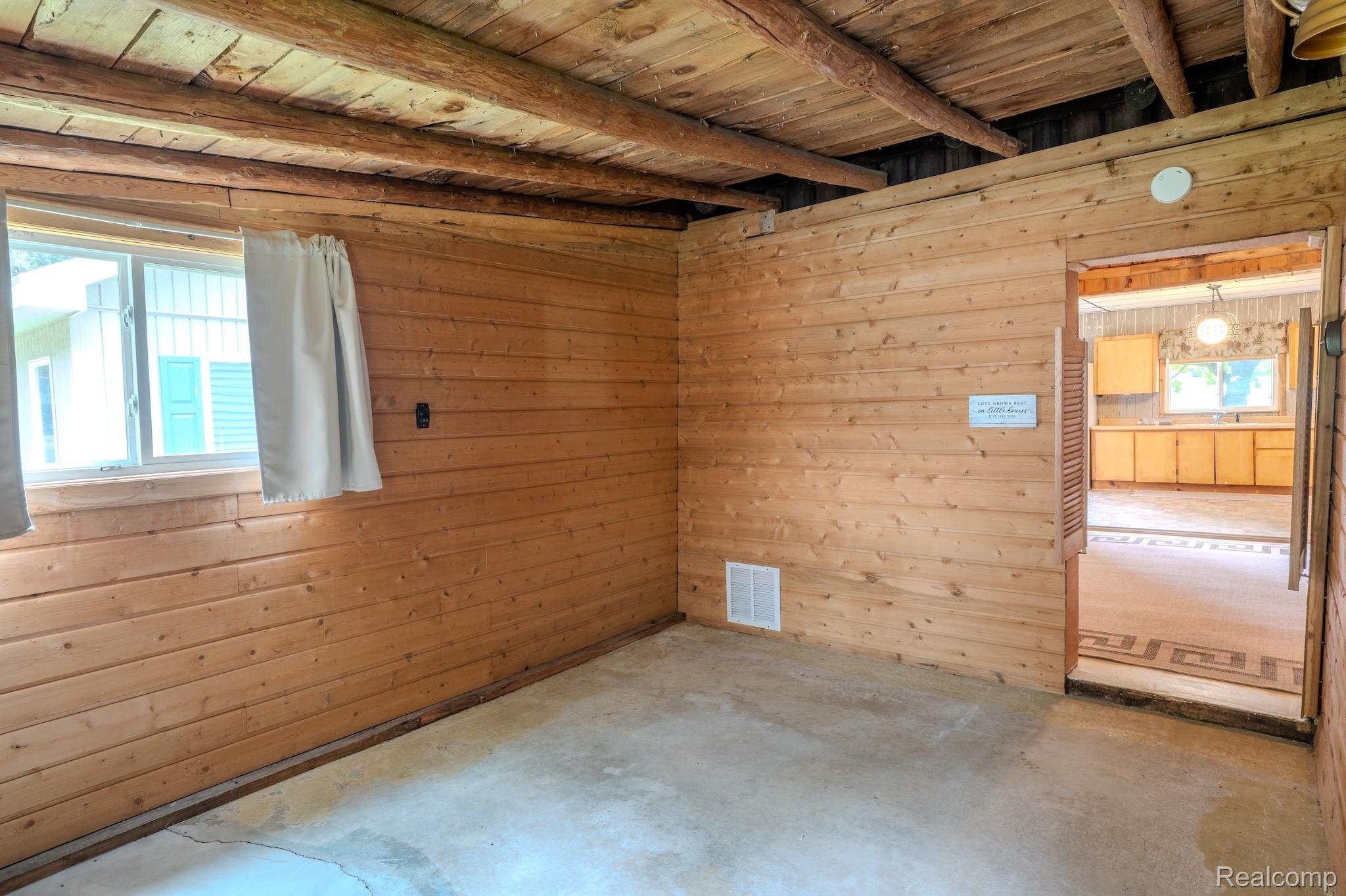 4350 Shrew Road Lincoln, MI 48742 - Photo 19 of 32 Room featuring wood-plank walls, exposed wood beam ceiling, concrete flooring, and a single window with white trim