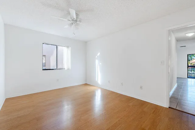 an empty room with wooden floor chandelier fan and windows