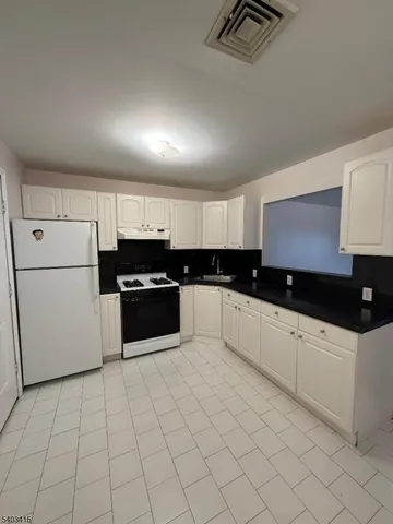 a kitchen with granite countertop a refrigerator sink and white cabinets