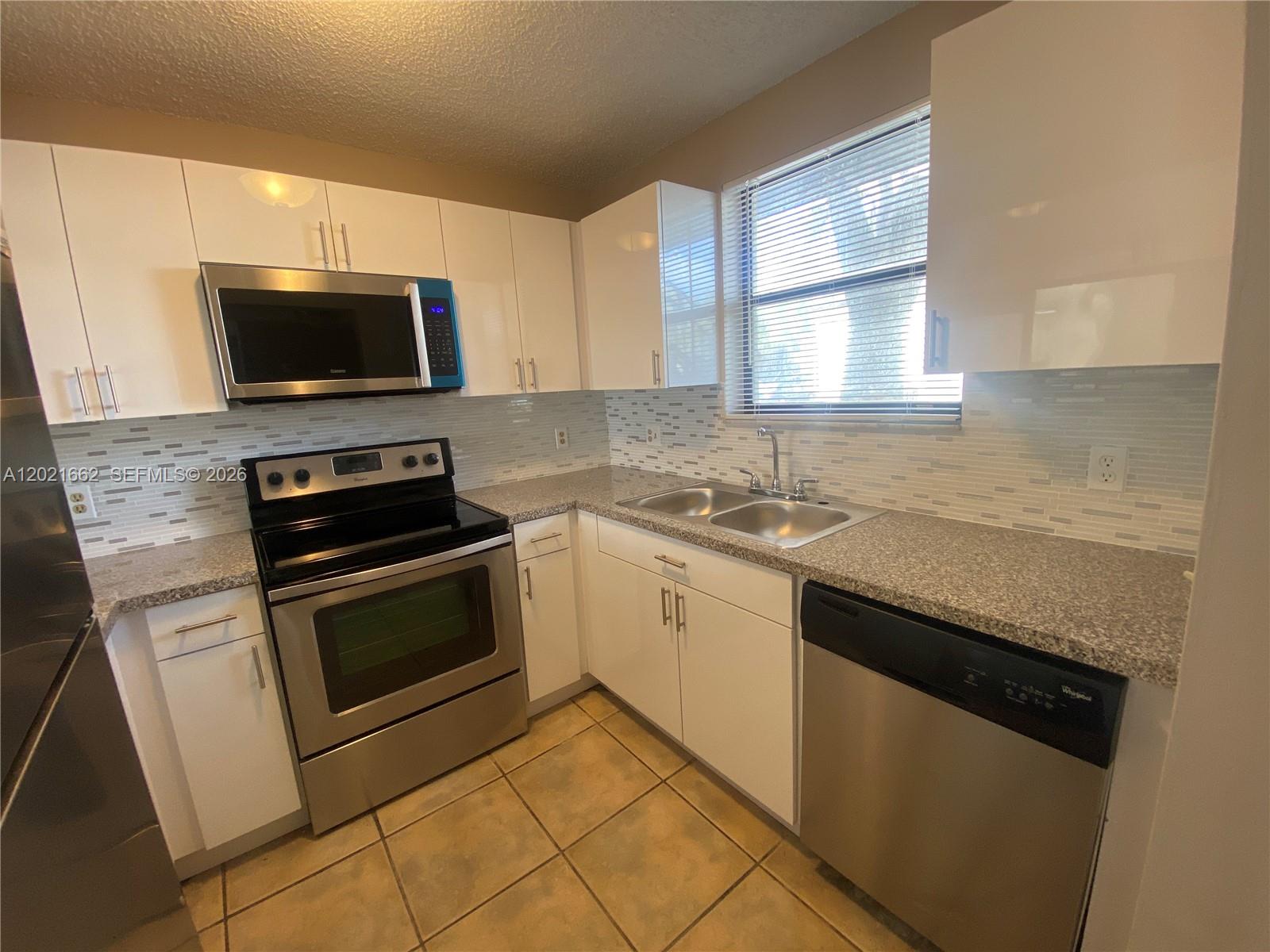 3263 Kirk Road, Unit 2 Lake Worth, FL 33461 - Photo 7 of 14 a kitchen with granite countertop a sink dishwasher stove and microwave with wooden cabinets