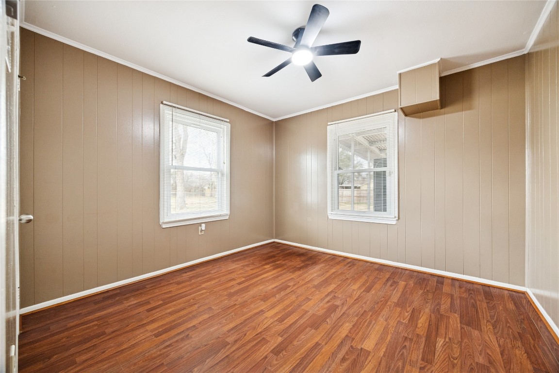 12537 Terrance Street Houston, TX 77085 - Photo 11 of 27 This secondary bedroom features warm wood-paneled walls and laminate flooring, with two large windows offering ample natural light. A modern ceiling fan provides overhead lighting and air circulation.