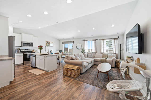 1175 Silver Hollow Road Syracuse, UT 84075 - Photo 8 of 34 Open concept living space featuring wood-finish flooring, vaulted ceiling, recessed lighting, and a kitchen with white cabinetry, stainless steel appliances, and an island with an undermount sink