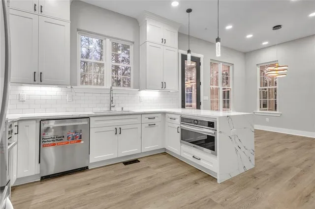 a kitchen with stainless steel appliances granite countertop a stove a sink and white cabinets with wooden floor