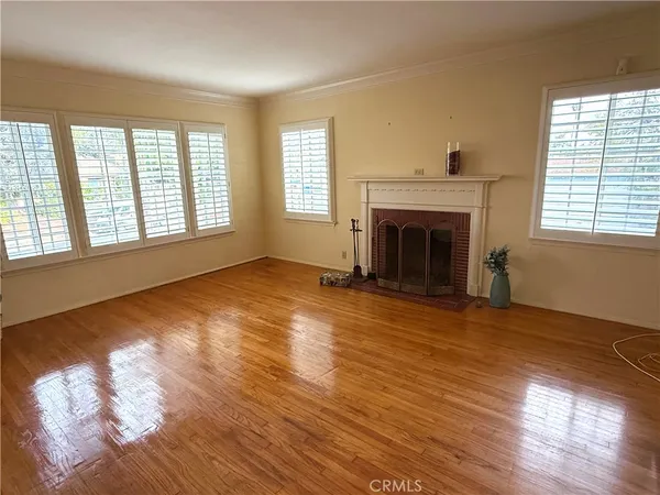 an empty room with wooden floor fireplace and windows