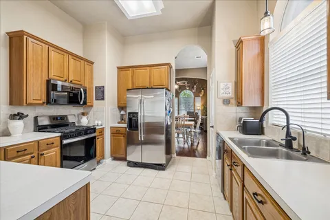 a kitchen with stainless steel appliances granite countertop a sink a stove top oven a refrigerator cabinets and a dining table with wooden floor