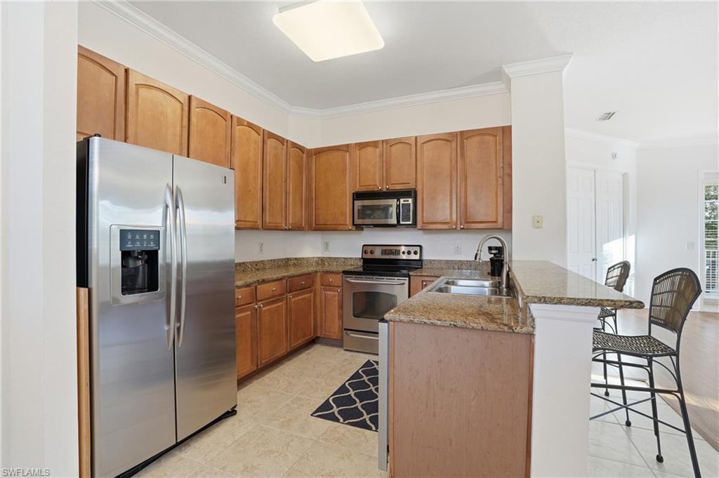 970 Peggy Circle, Unit 604 Naples, FL 34113 - Photo 15 of 24 Kitchen featuring stainless steel appliances, a peninsula, ornamental molding, dark stone countertops, and a breakfast bar area