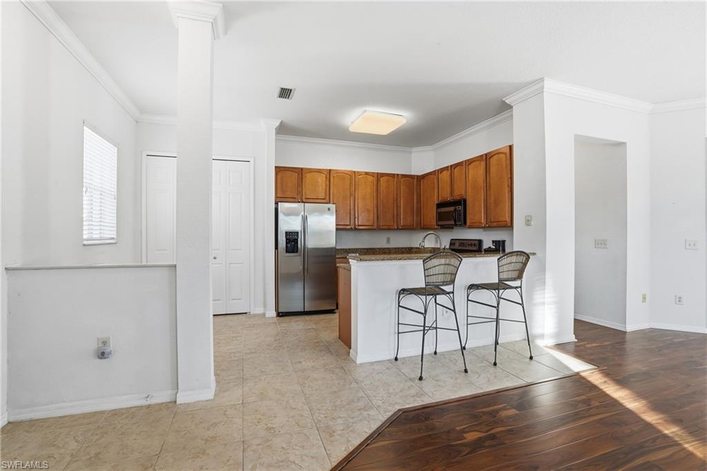 970 Peggy Circle, Unit 604 Naples, FL 34113 - Photo 3 of 24 Kitchen with crown molding, a breakfast bar, appliances with stainless steel finishes, brown cabinetry, and dark stone counters