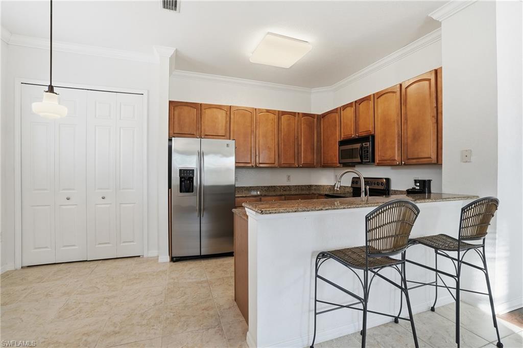 970 Peggy Circle, Unit 604 Naples, FL 34113 - Photo 8 of 24 Kitchen featuring brown cabinetry, dark stone counters, black appliances, ornamental molding, and a peninsula