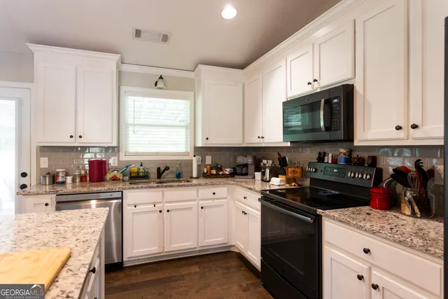a kitchen with stainless steel appliances granite countertop white cabinets sink and window